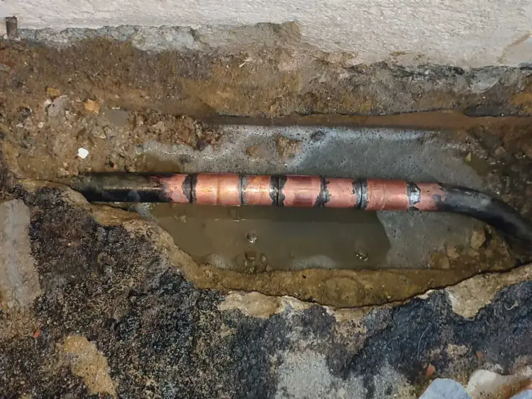 A leaking copper heating pipe uncovered in the wet floor of a kitchen